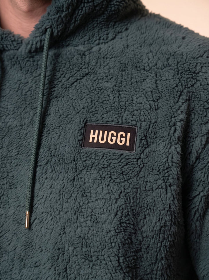 Close-up of the HUGGI logo patch on the Dark Green sherpa fleece hoodie
