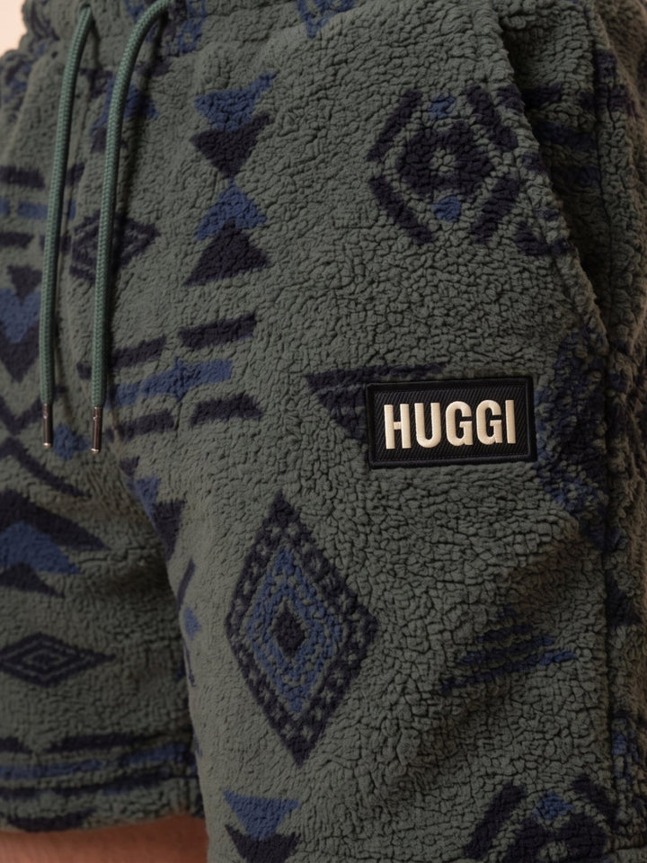Close-up of the HUGGI logo patch on the Green &amp; Black fleece shorts